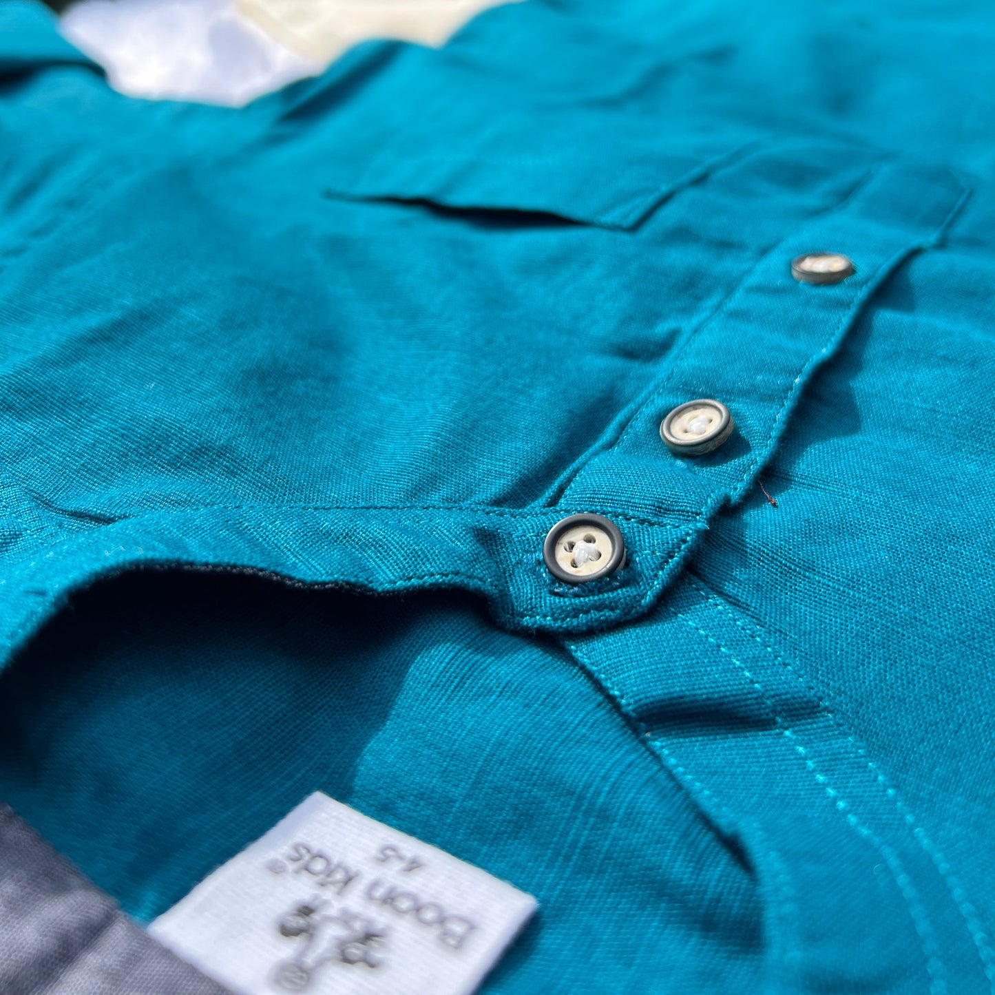 Close-up of a teal shirt with buttons and a brand label, blurred background