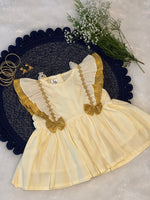 Children's dress with gold accents on a textured surface with flowers and jewelry.