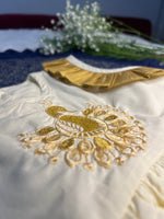 White garment with gold embroidery and a small bouquet of white flowers on a blue surface.