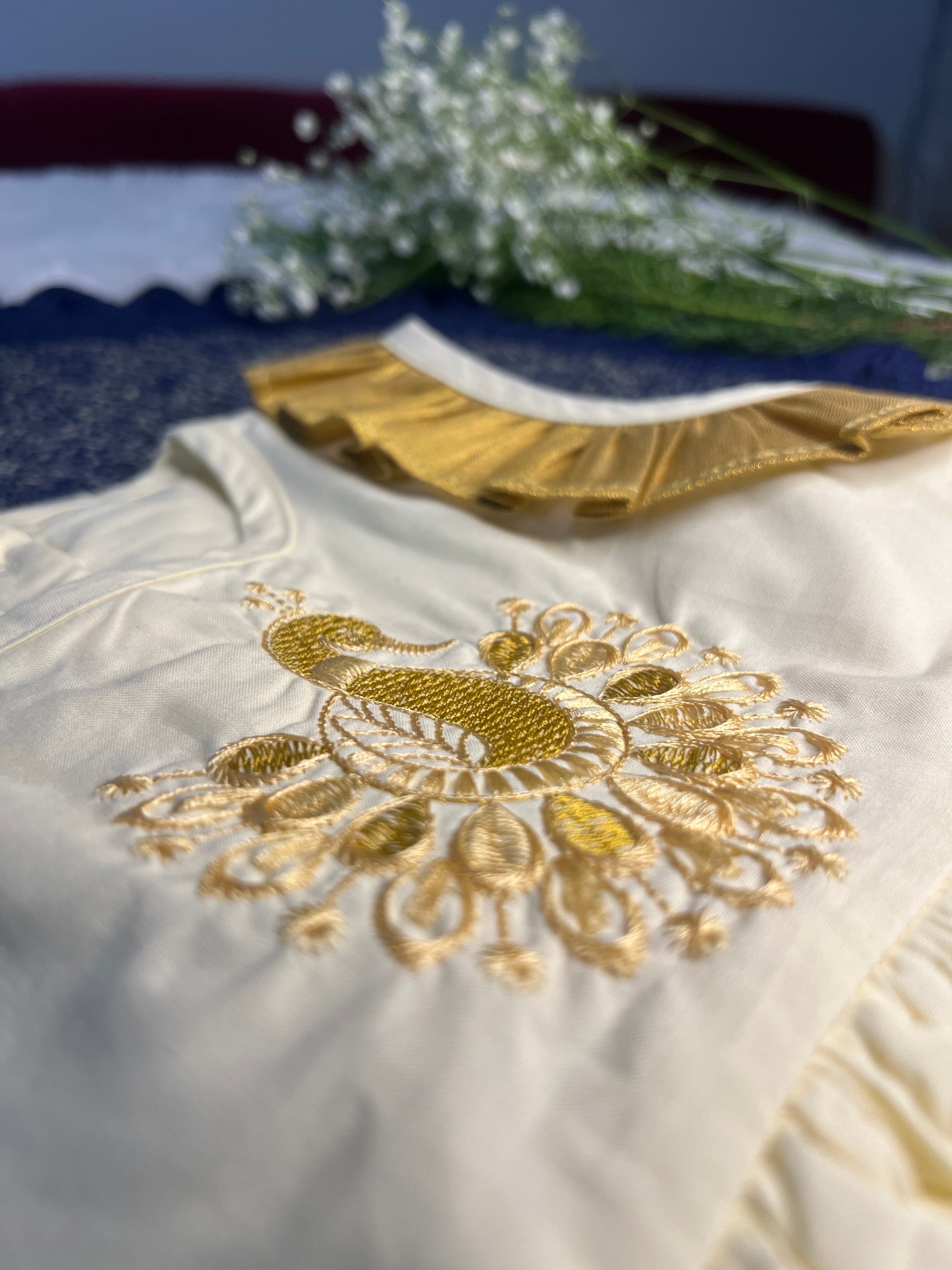 White garment with gold embroidery and a small bouquet of white flowers on a blue surface.