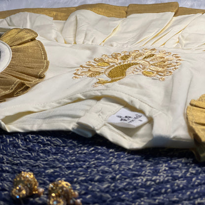 White garment with gold embroidery on a blue textured surface, accompanied by gold jewelry.