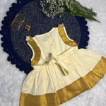 Children's outfit with white top and gold trim on a textured surface with flowers and jewelry.