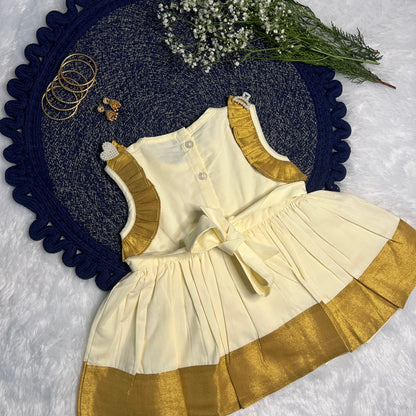 Children's outfit with white top and gold trim on a textured surface with flowers and jewelry.