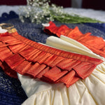 Close-up of a garment with red ruffled details on a blue fabric background.