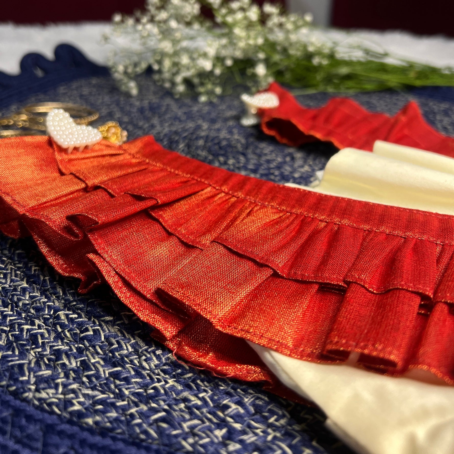 Red ruffled dress on a blue textured surface with white flowers in the background