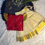 Traditional outfit with red blouse and white saree with gold border on a textured surface.