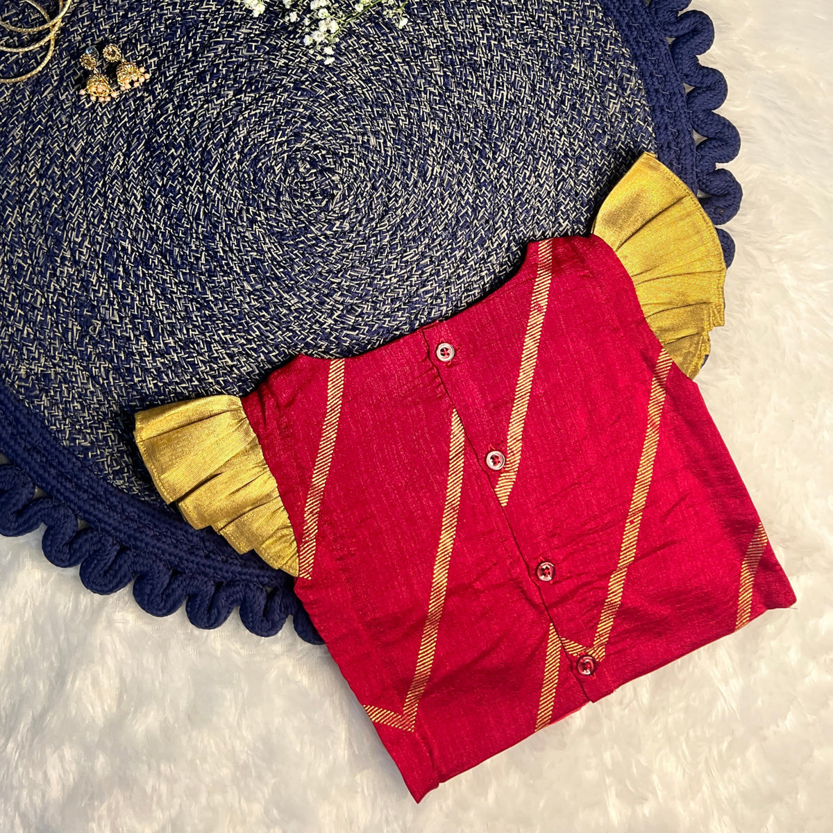  red top, gold jewelry, and white flowers on a textured surface.