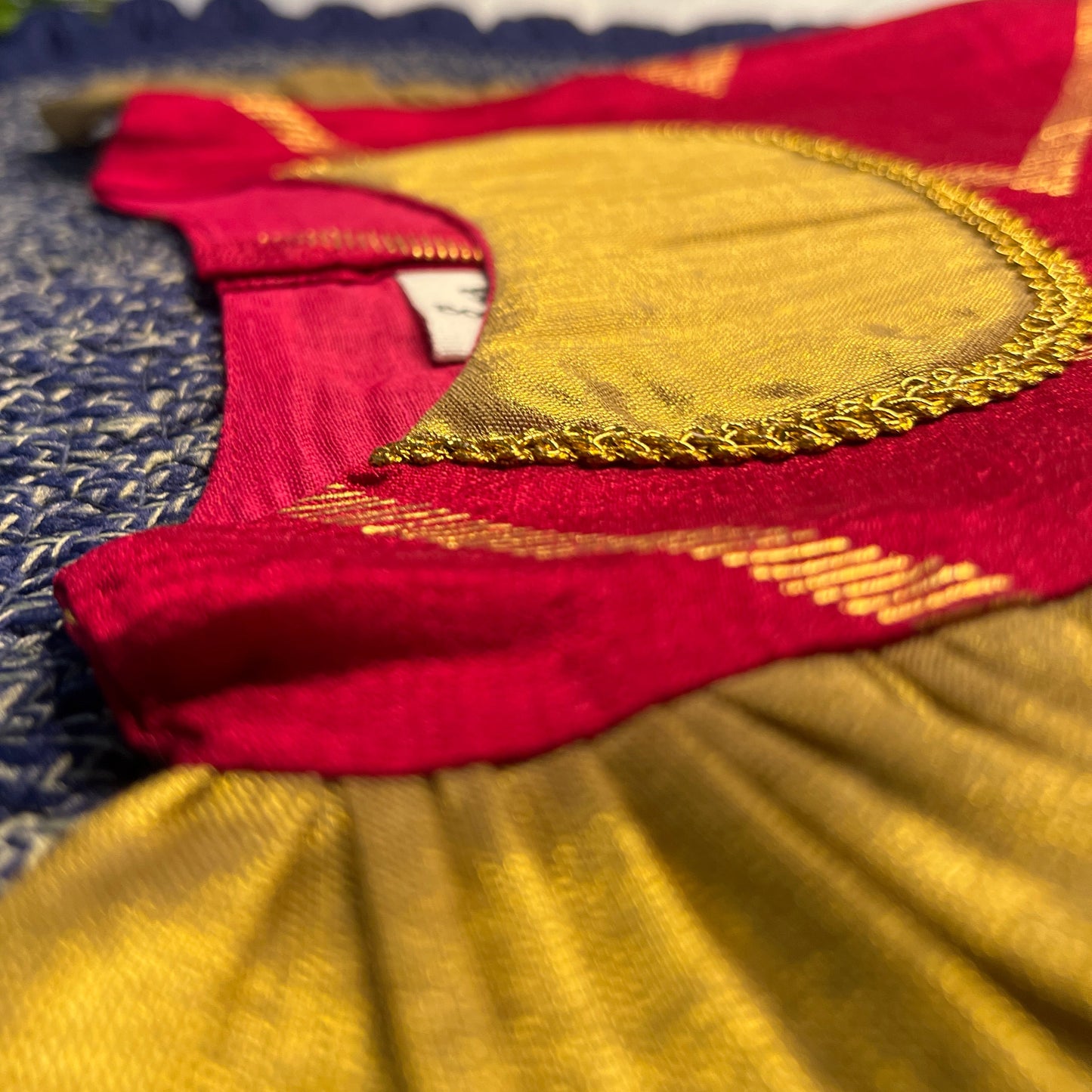 Close-up of a traditional red and gold fabric with intricate patterns on a blue background.