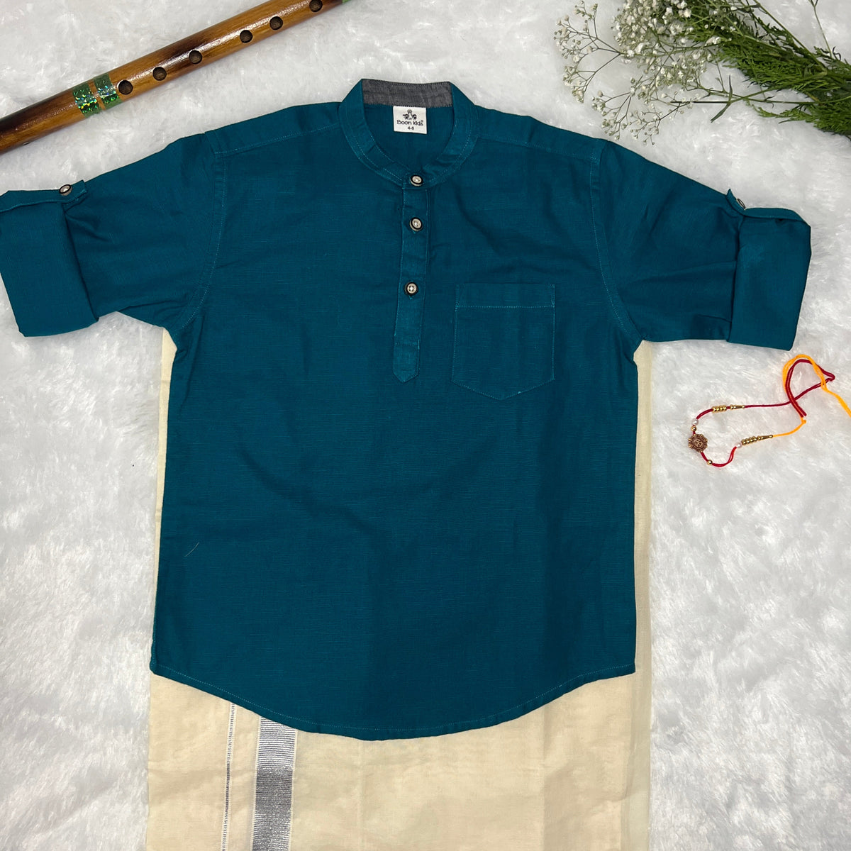 Teal shirt on a white dhothi with background with a plant and bamboo stick.