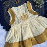 Beige and gold dress with embroidery on a textured blue surface with jewelry and flowers.