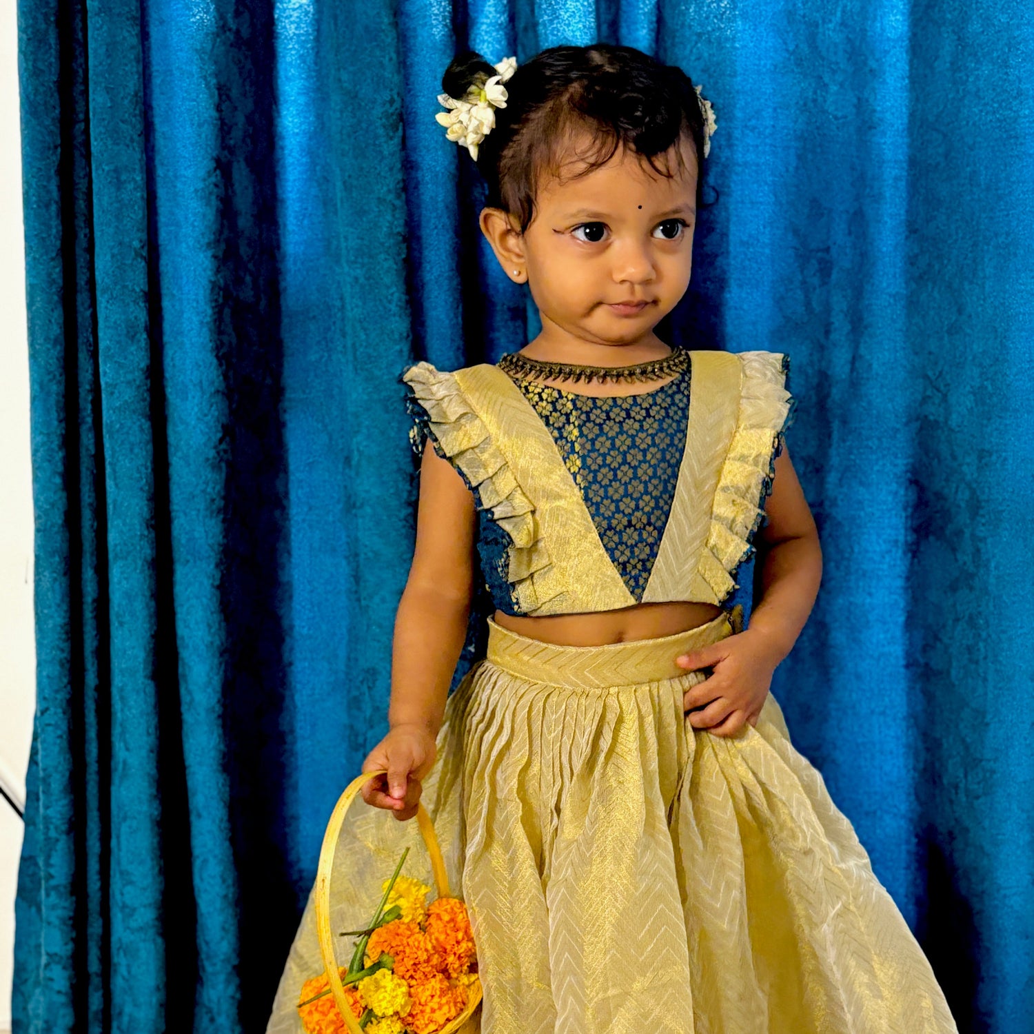 Child in a traditional outfit holding flowers against a blue curtain