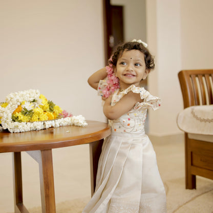 Young girl in a white dress standing next to a table with flowers indoors.