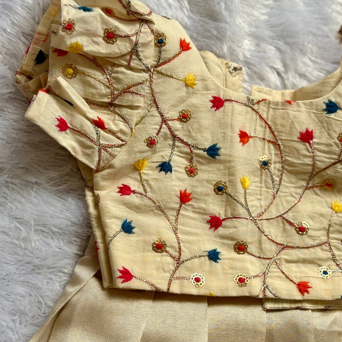 Beige embroidered fabric with colorful patterns on a white textured background