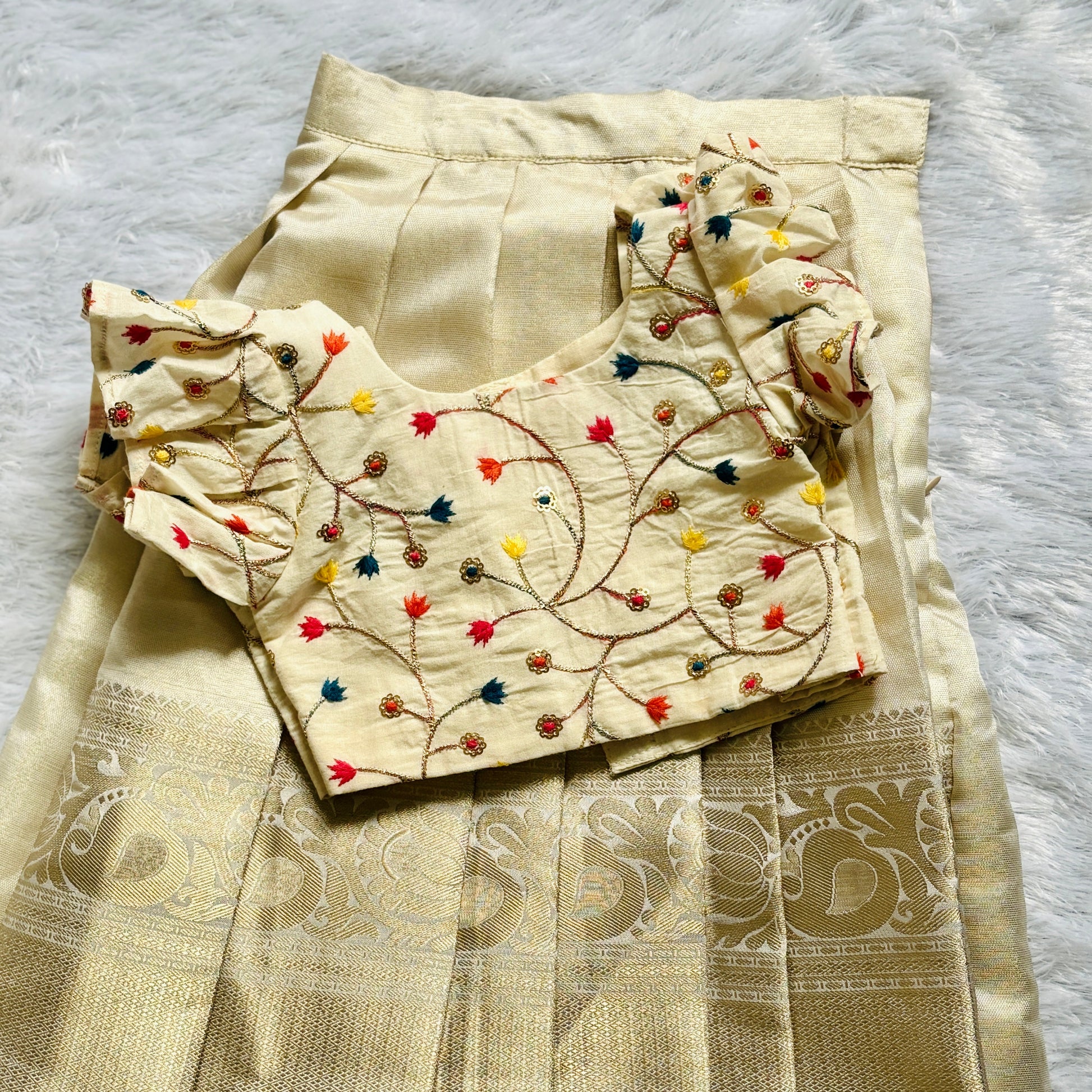 Beige embroidered blouse and saree with intricate patterns on a light gray background